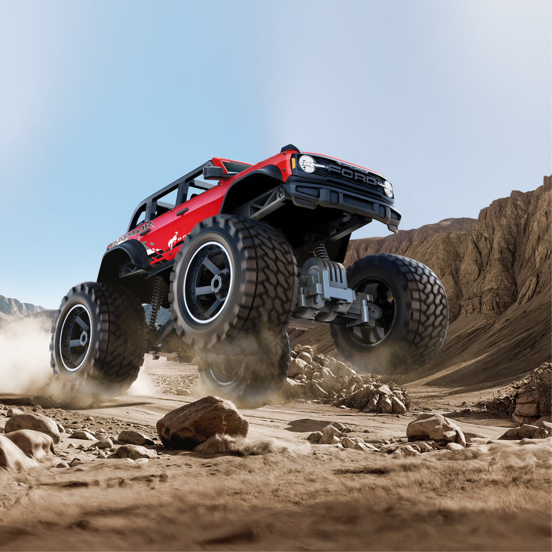 Red off-road vehicle with large tires driving on a rocky desert landscape