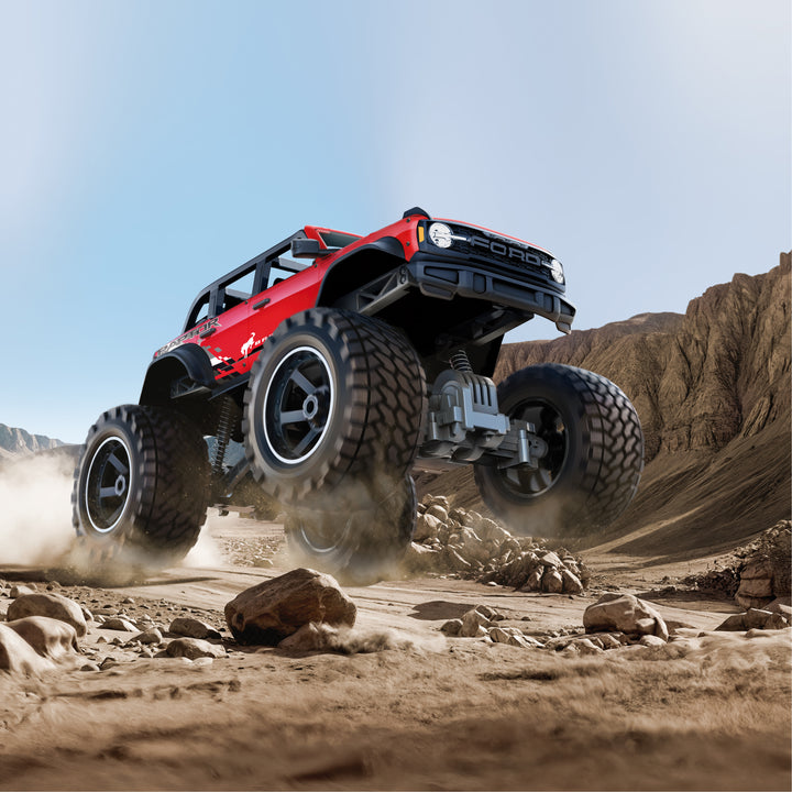 Red off-road vehicle with large tires driving on a rocky desert landscape