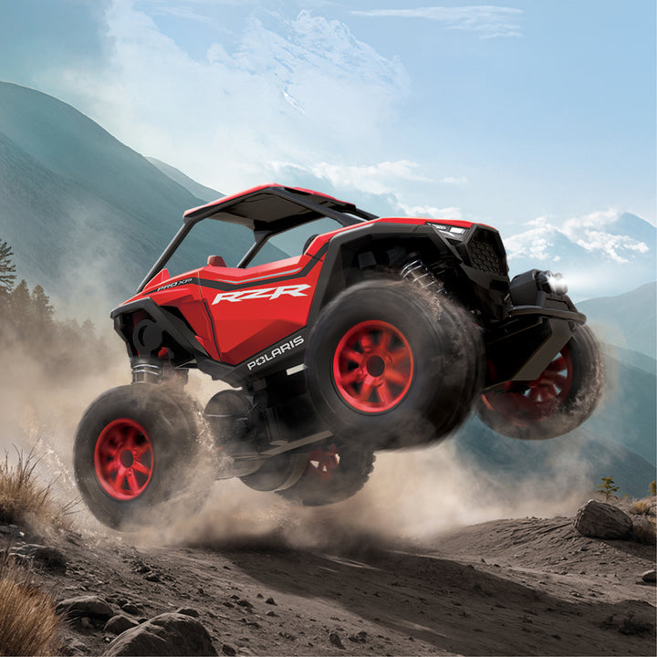 Red Polaris RZR off-road vehicle in action on a dirt trail with mountains in the background